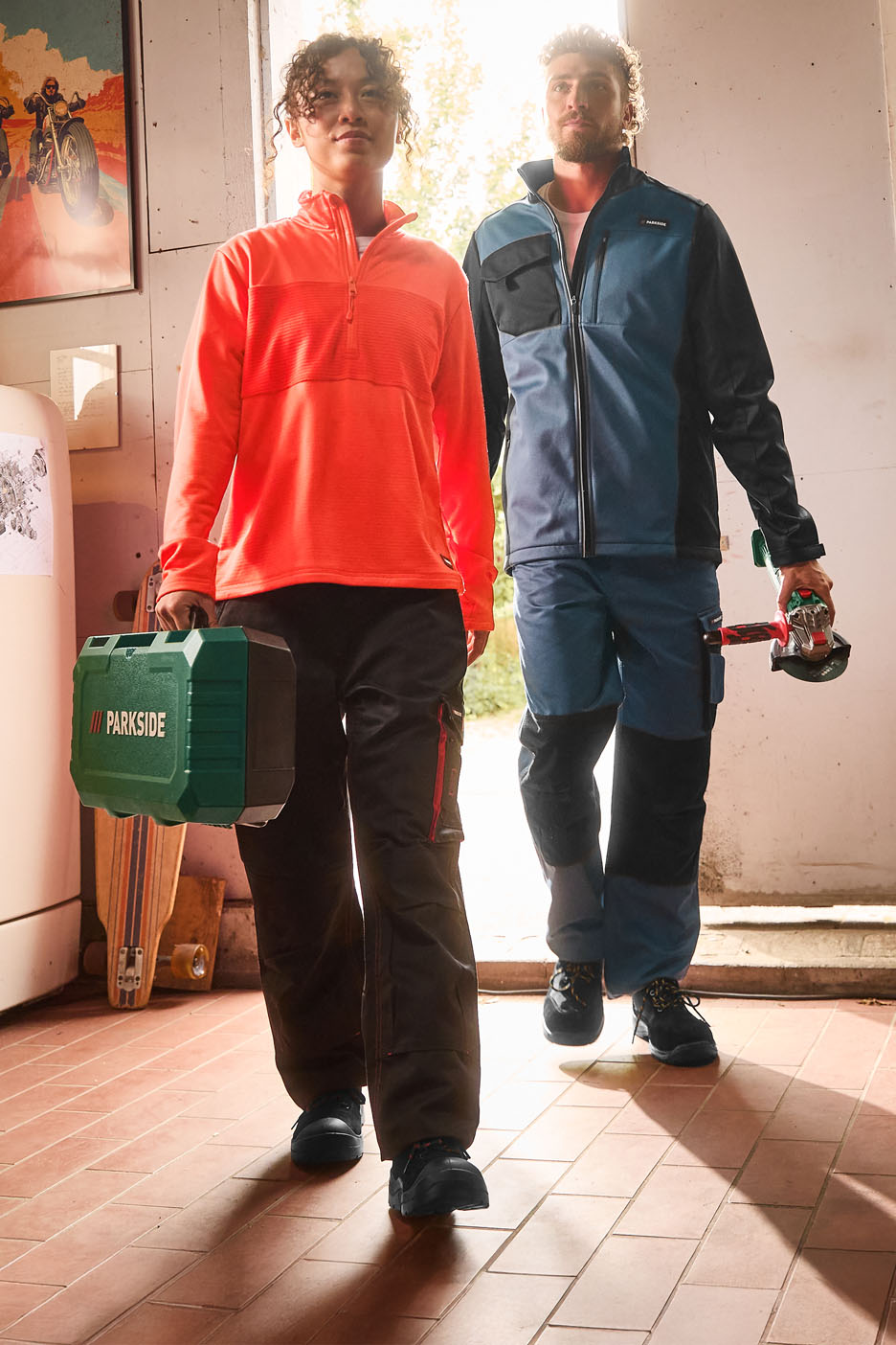 Two people in workwear, with tools and a toolbox, walking on tiled flooring.