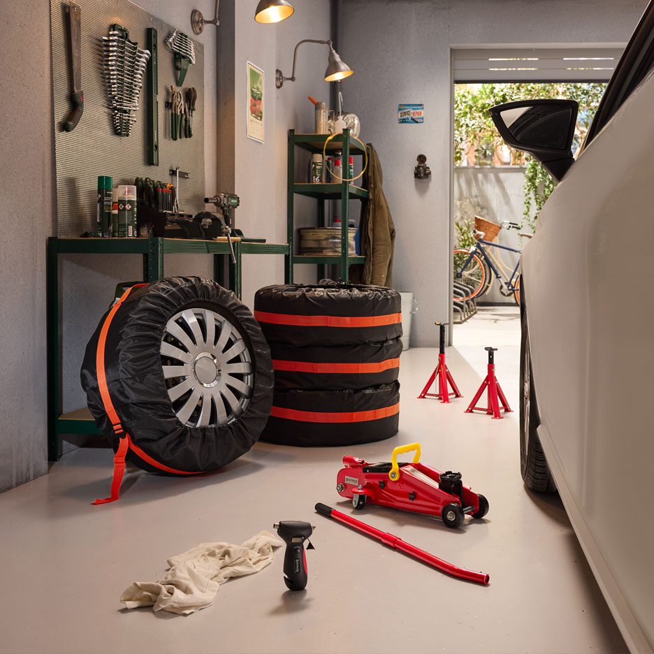 Garage with tires in covers, jack, and jack stands, ready for tire change.