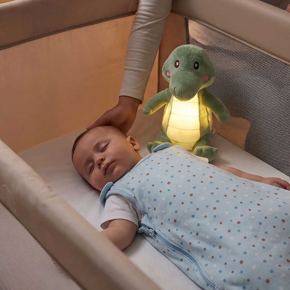 Baby sleeping in cot, with a crocodile-shaped night light.