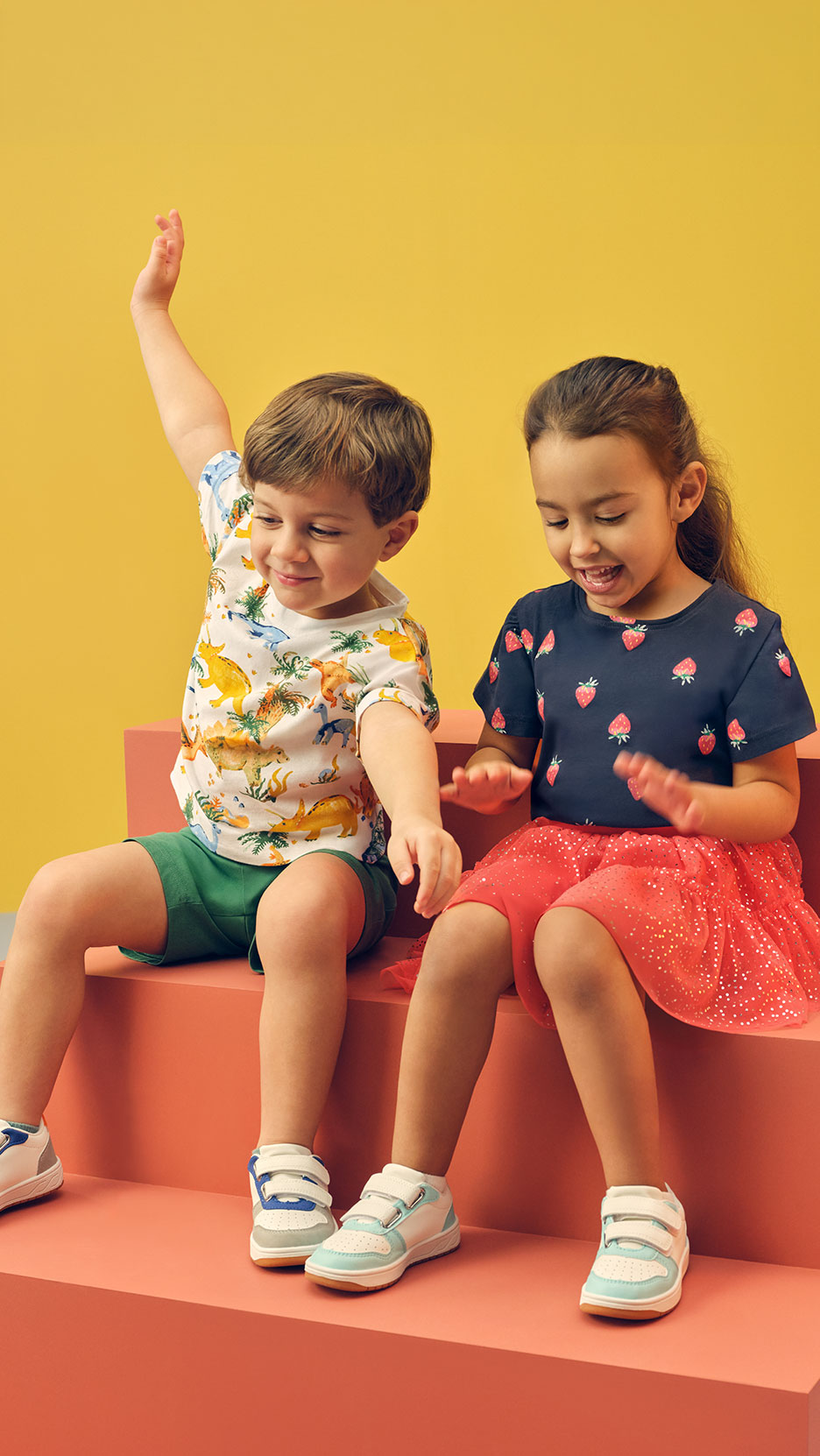 Two children in summer clothes and sneakers sitting on orange steps, playing.