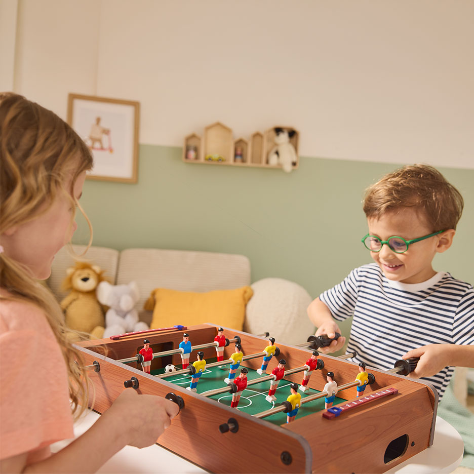 Two children playing table football in a living room.