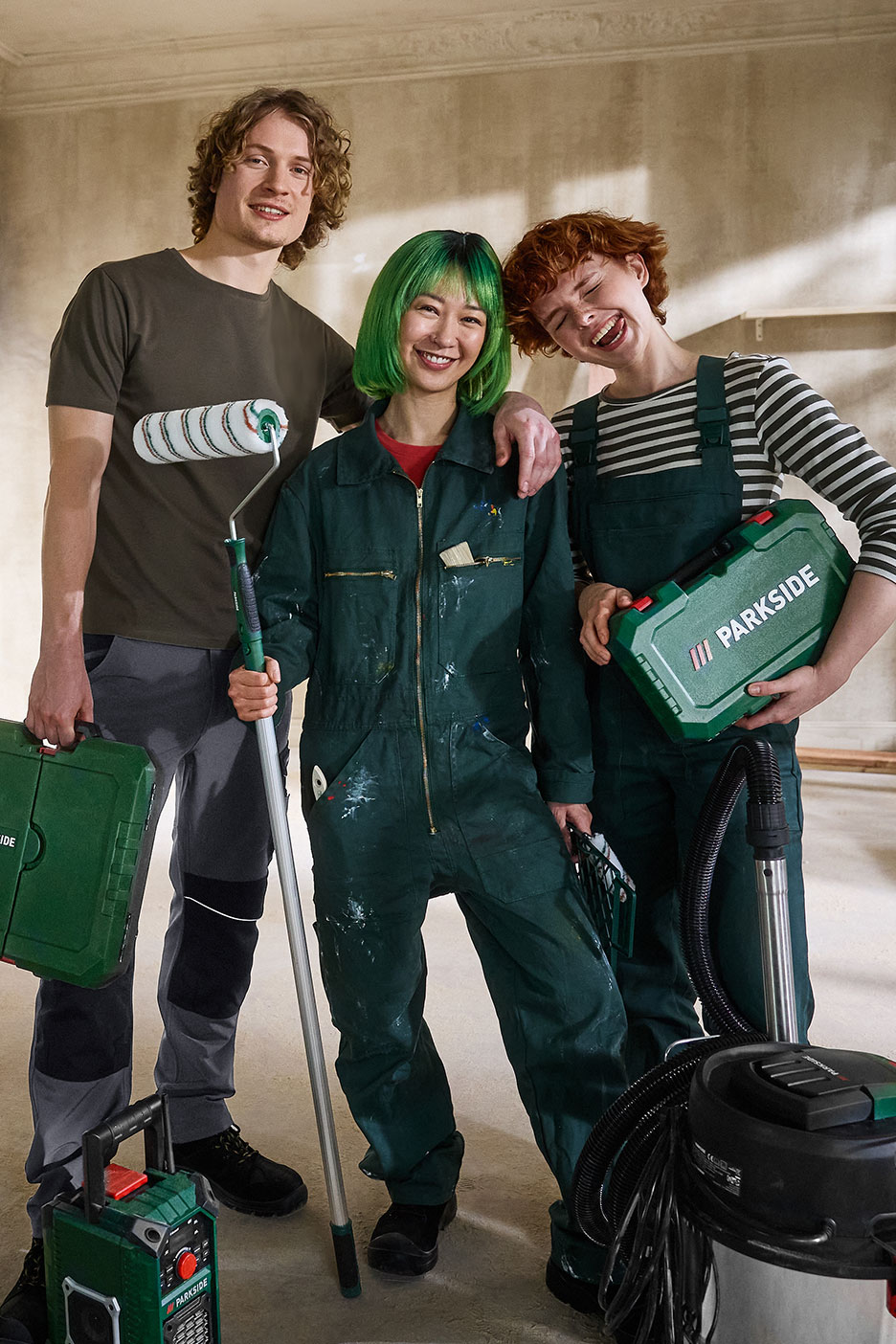 Three smiling people with renovation tools, including a paint roller and a toolbox.