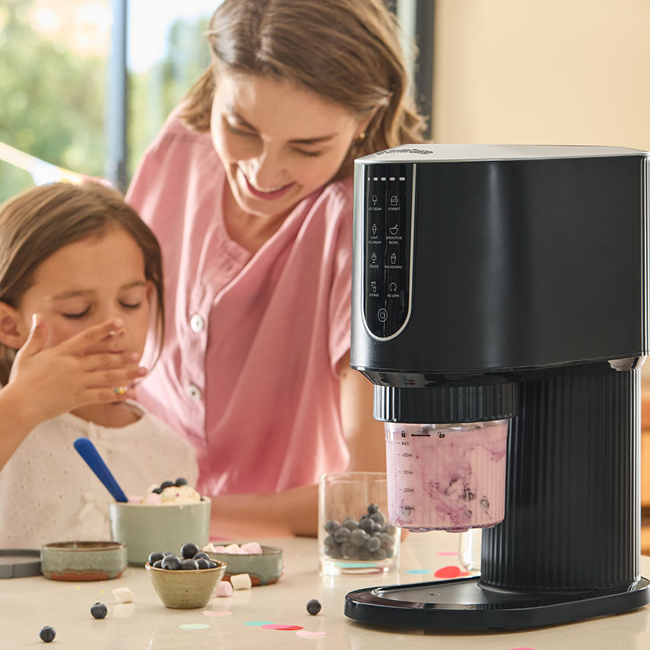 Black ice cream maker with a girl and smiling woman preparing blueberry dessert.