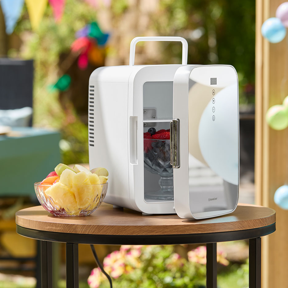 White portable mini-fridge with fresh fruit on a garden table.