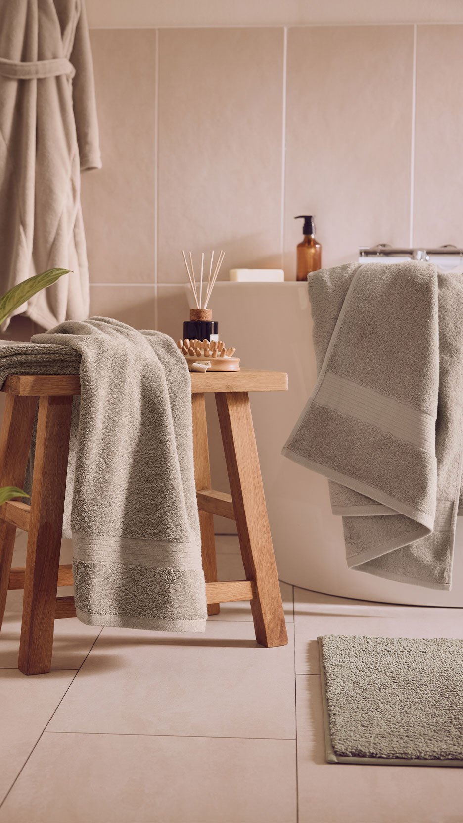 Bathroom with light green towels, bath mat, and a wooden stool.