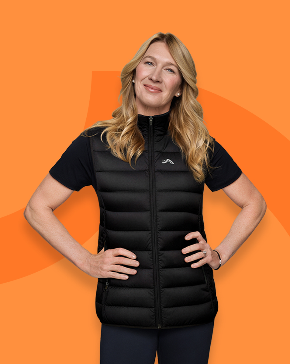 Woman in a black puffer vest and t-shirt, hands on hips, smiling.