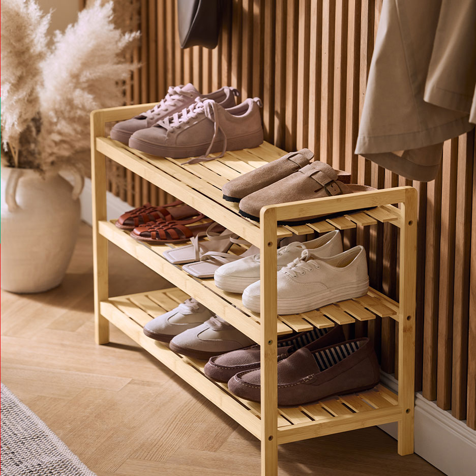 Three-tier bamboo shoe rack with women's and men's shoes, a vase, and a coat.