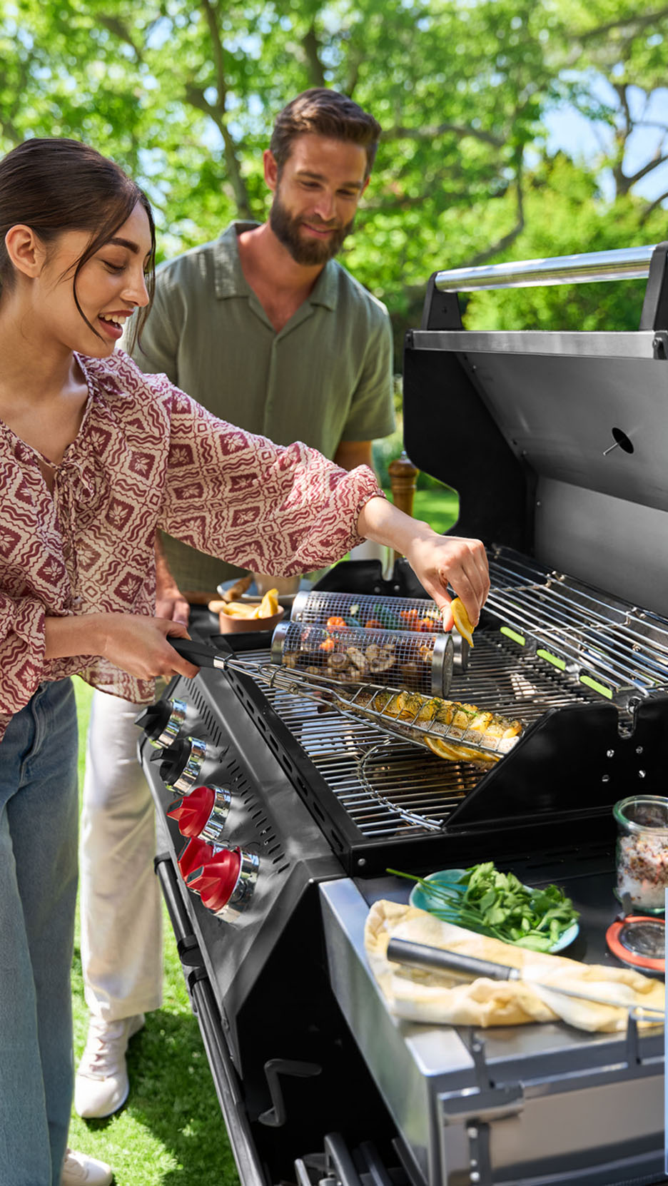 Couple grilling fish and vegetables on a gas grill in the garden.