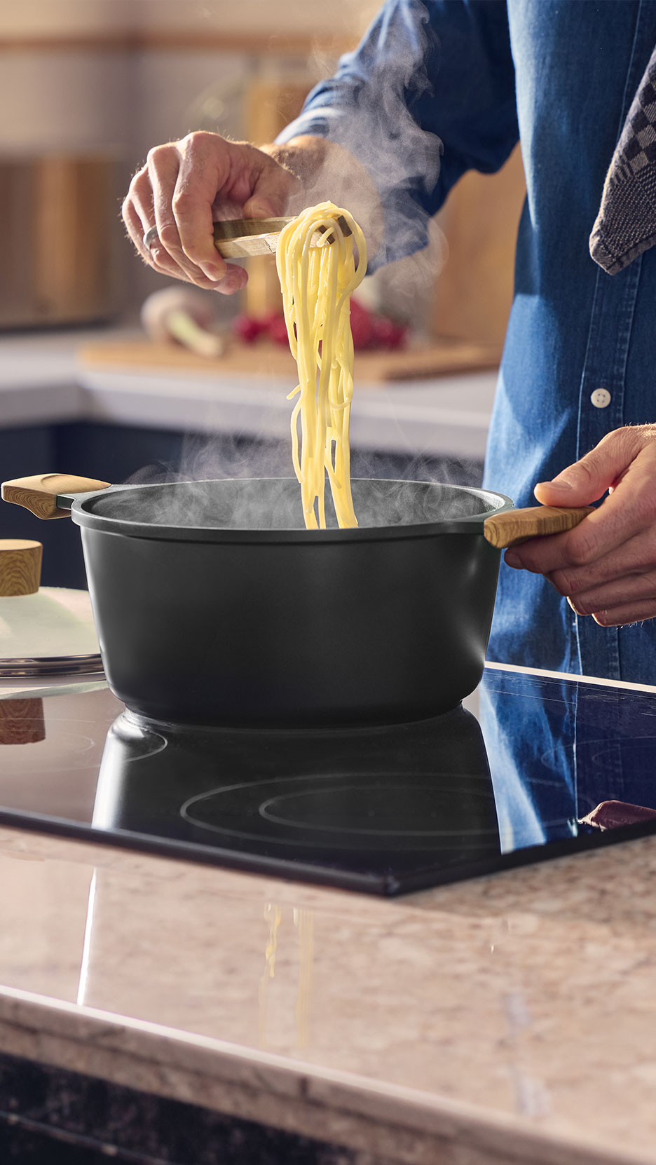 Man cooking spaghetti in a black pot on an induction hob.