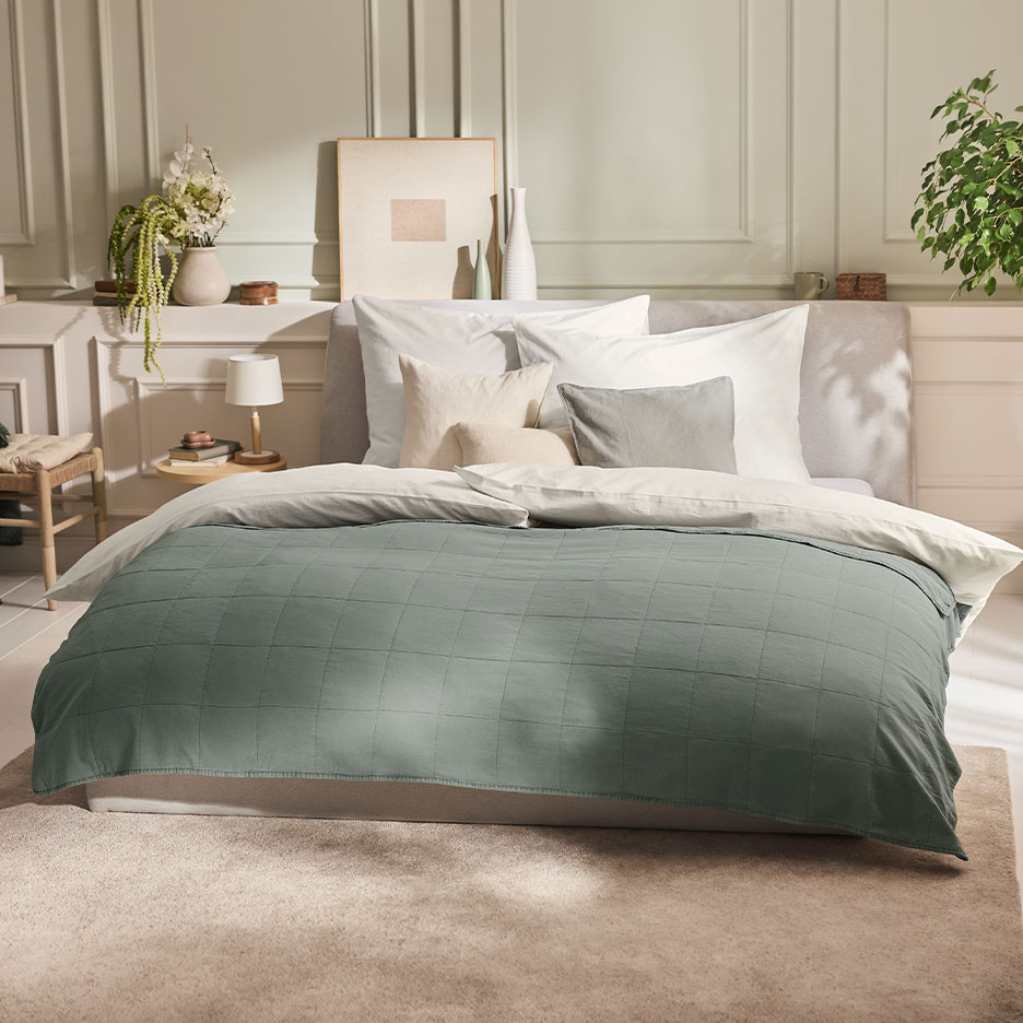 Bedroom with a bed featuring a green quilted bedspread and white bedding.