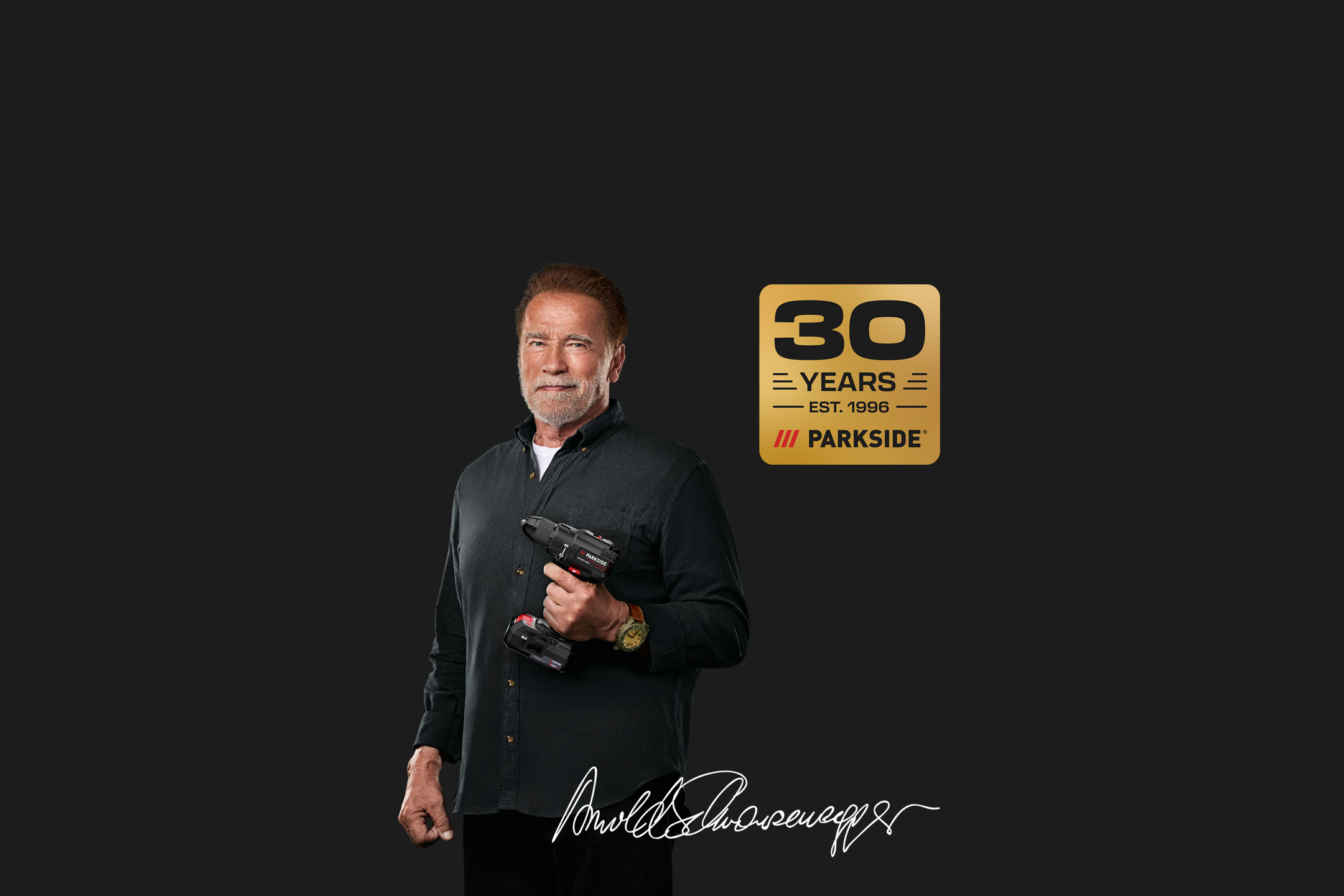 Arnold Schwarzenegger holds a cordless drill, with a '30 YEARS' logo and his signature.