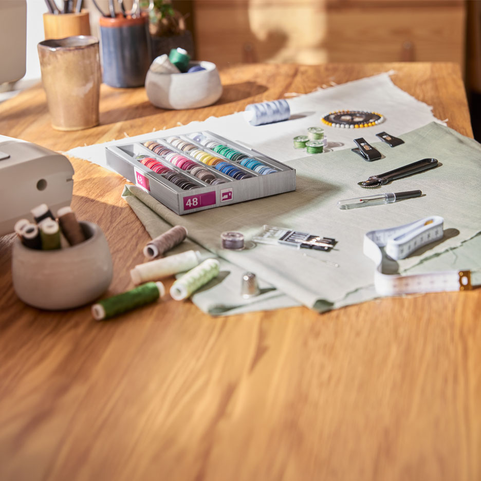 Wooden table with a box of colorful sewing threads, fabrics, and sewing accessories.