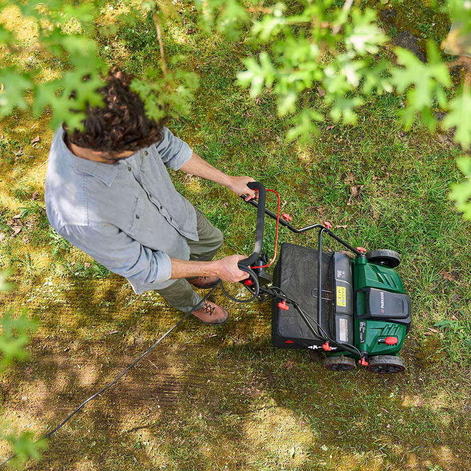 Man mowing grass with a green lawnmower, overhead view.